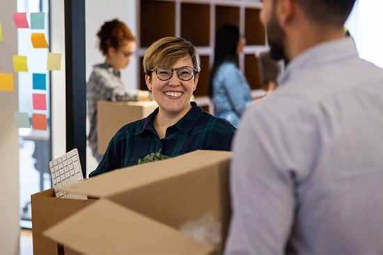 Female and male colleagues holding moving boxes in an office;